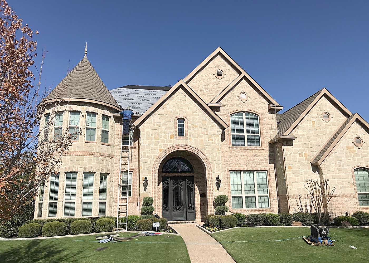 A brick home with ladders up and material stacked on the lawn