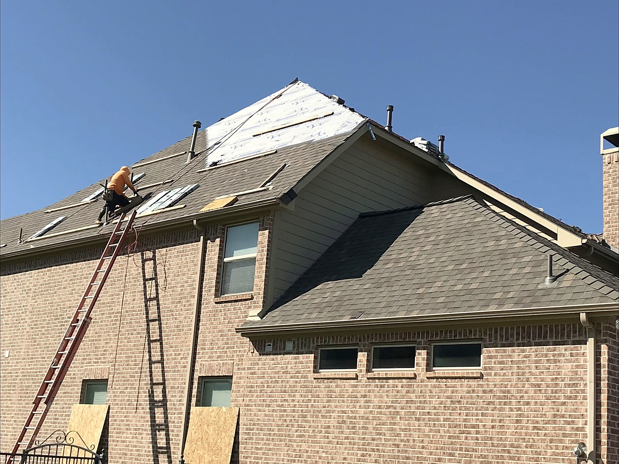 A GreyHawk roofer at work on a two-story brick home, ladders up against the wall