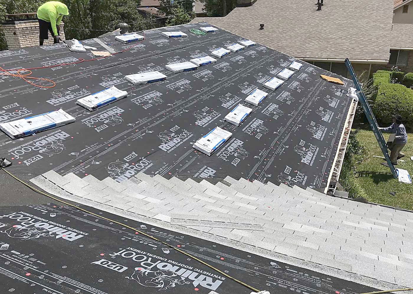 Underlayment half laid across a big roof with the crew working